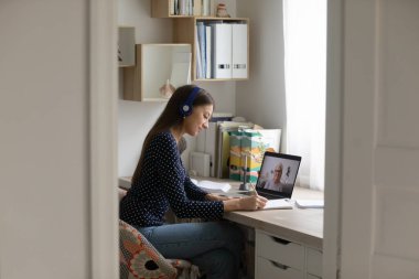 Ciddi kadın öğrenci kulaklık takıyor, internetten ders çalışıyor, video görüşmesi yapıyor.