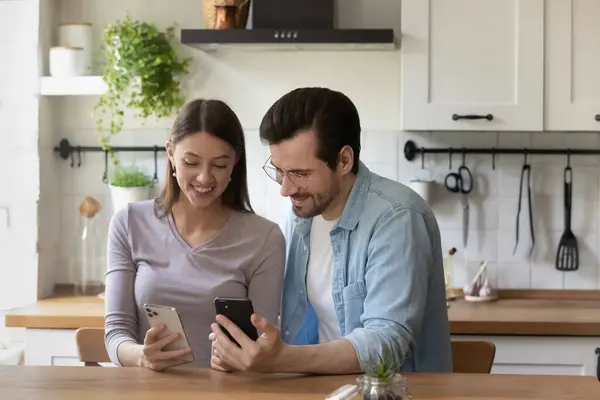 Akıllı telefon kullanan, mutfaktaki masada oturan mutlu genç çift. — Stok fotoğraf