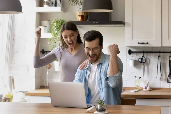 Overjoyed couple looking at laptop screen, celebrating success
