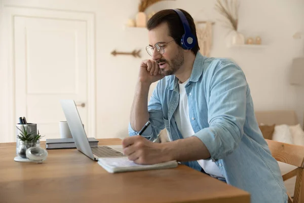 Serious man wearing glasses using laptop, writing notes, working online — Stock Photo, Image