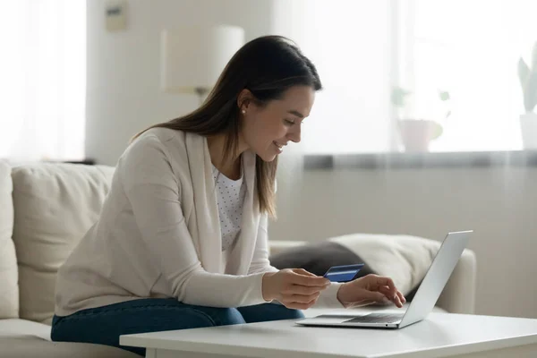 Улыбающаяся молодая женщина с помощью ноутбука, платит онлайн кредитной картой — стоковое фото