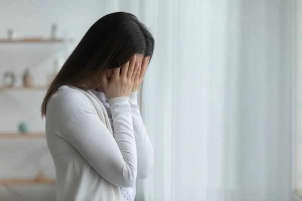 Нещасна жінка, що прикриває обличчя руками, плаче вдома сама — стокове фото