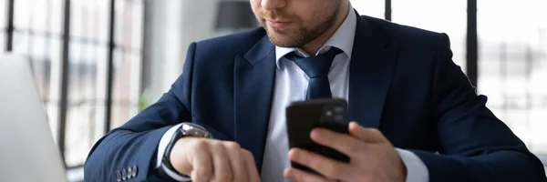 Horisontell banner säker affärsman tittar på armbandsur, håller smartphone — Stockfoto
