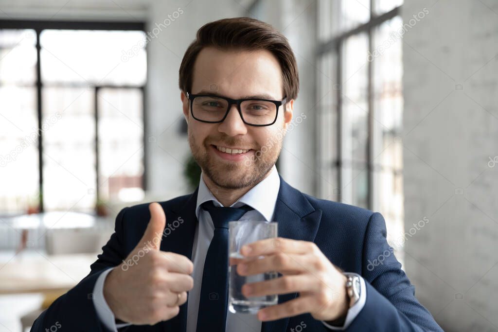 Head shot portrait smiling businessman showing thumb up, drinking water