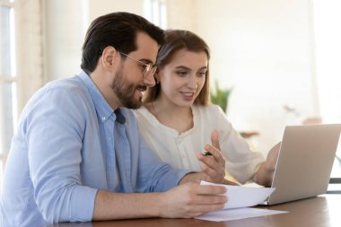 Gülümseyen meslektaşlar laptopta iş birliği yapıyorlar.