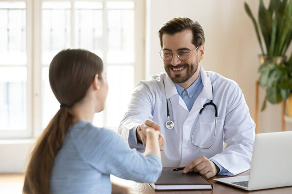 Smiling male doctor handshake female patient at consultation
