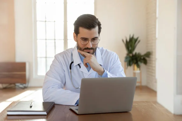 Thoughtful male GP work on computer in clinic