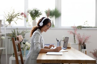 Masada oturan, kulaklıklı kadın tasarımcı evrak işlerine odaklanmış.