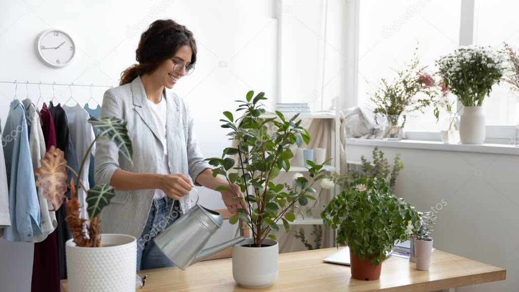 Positive millennial woman office manager starting workday by watering flowers