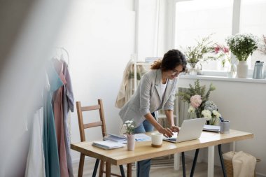 Motive olmuş genç bayan giyim tasarımcısı dizüstü bilgisayarın yanında e-posta yazdırıyor