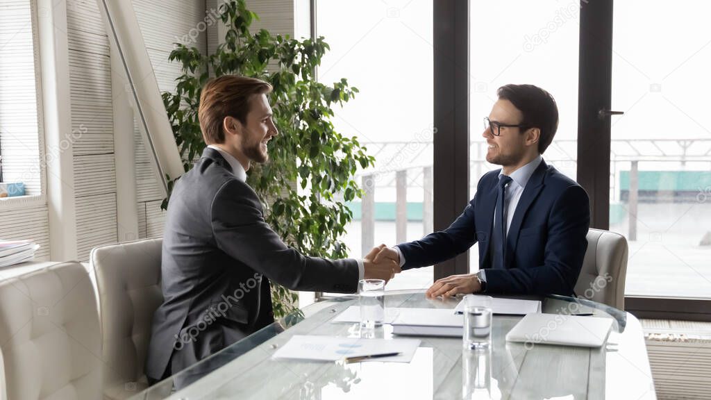 Smiling male business partners handshake at office meeting