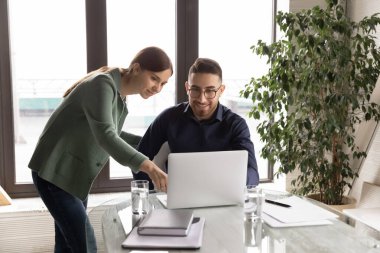 Gülümseyen çok ırklı meslektaşlar dizüstü bilgisayarda birlikte çalışıyorlar