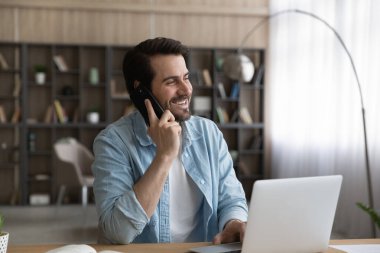 Mutlu adam bilgisayar başında çalışıyor. Akıllı telefondan konuşuyor.