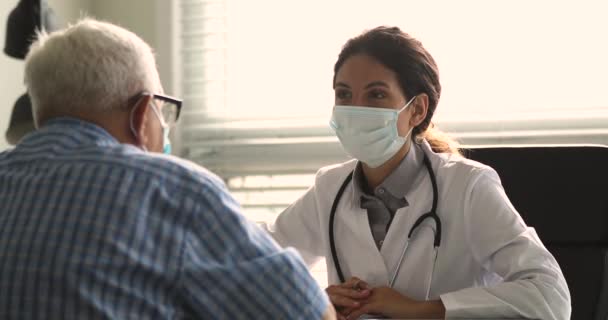Therapeut trägt Gesichtsmaske im Gespräch mit älteren Patienten während des Besuchs — Stockvideo