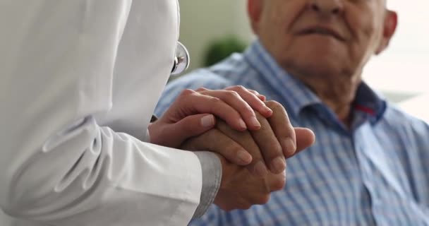 Médico femenino que sostiene la mano masculina mayor del paciente expresan apoyo, primer plano — Vídeos de Stock