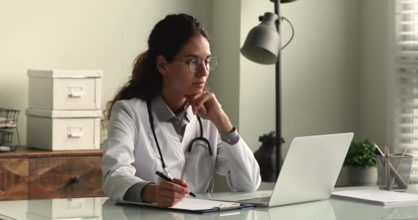 Jeune femme médecin en uniforme médical blanc travaillant sur ordinateur portable — Video