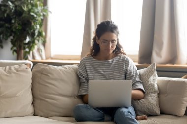 Kafkasyalı kadın bilgisayar kullanarak kanepeye oturur.