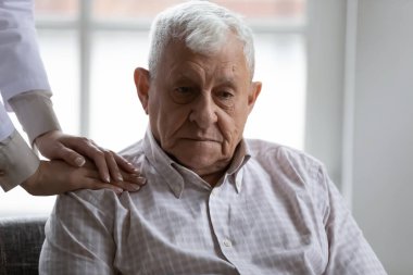 Doktor, bunama geçiren yaşlı bir hastanın omuzlarında ellerini gezdiriyor.
