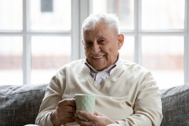 Mutlu yaşlı adam kanepede dinleniyor. Bir fincan çayın tadını çıkarıyor.