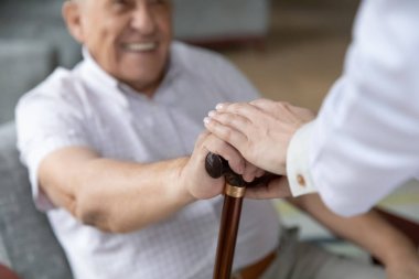 Hemşire avuç içi, elinde baston tutan gülümseyen yaşlı bir hastanın elini örtüyor.