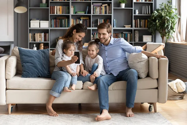 Happy rodiče relaxovat doma pomocí smartphonu s malými dětmi — Stock fotografie