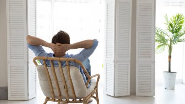 Arkadan bakan genç beyaz adam rahat koltukta dinleniyor..