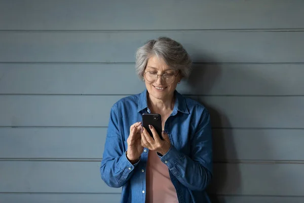 Улыбающаяся женщина 60-х годов в очках с помощью смартфона. — стоковое фото