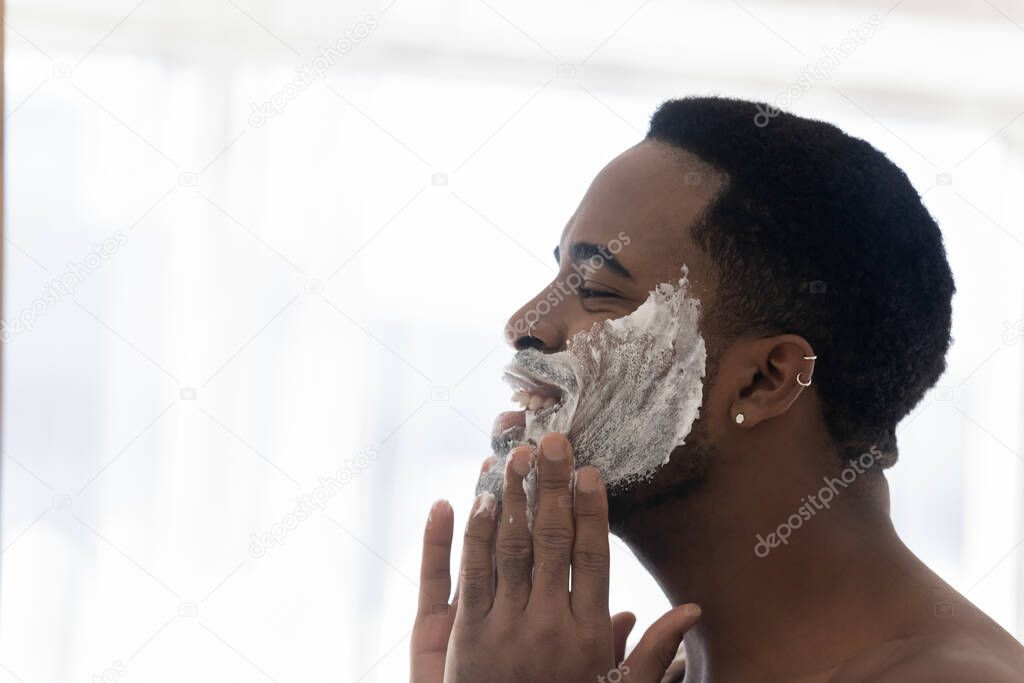 Happy young mixed race man cleansing face with foamy scrub.