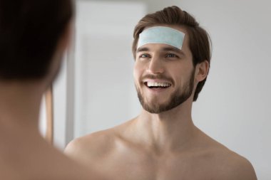 Happy young handsome man applying moisturizing patch on forehead. clipart