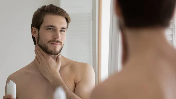 Pleasant young handsome caucasian man applying moisturizing lotion. — Stock Photo, Image