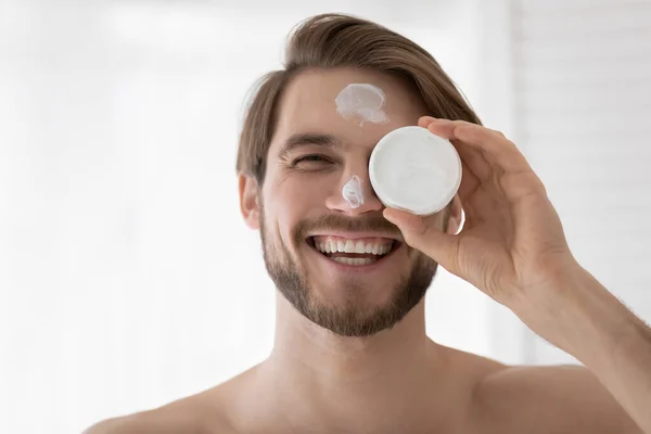 Happy young handsome man applying moisturizing cream. — Stock Photo, Image