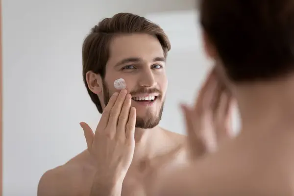 Smiling handsome man applying moisturizing creme in bathroom. — Stock Photo, Image