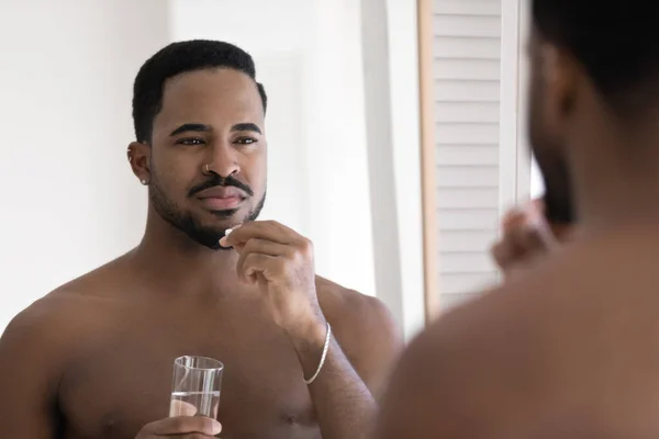 Young handsome african ethnicity 30s bare man taking pills. — Stock Photo, Image