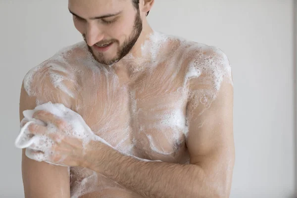 Happy young bare man cleaning body with foamy moisturizing gel. — Stock Photo, Image