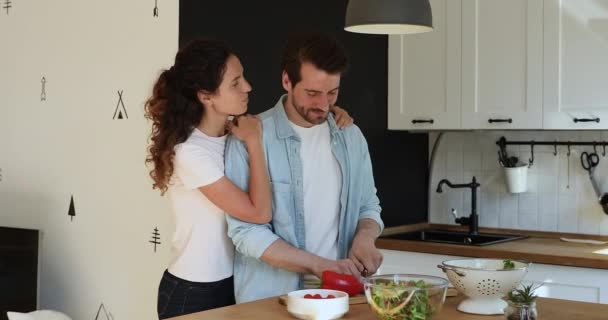 Usmívající se mladá žena objímající pohledný manžel připravuje jídlo. — Stock video