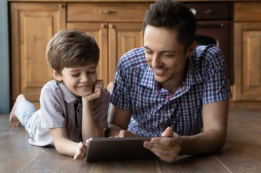 Büyük ve küçük kardeşler evde tablet kullanarak video oyunu oynuyorlar.