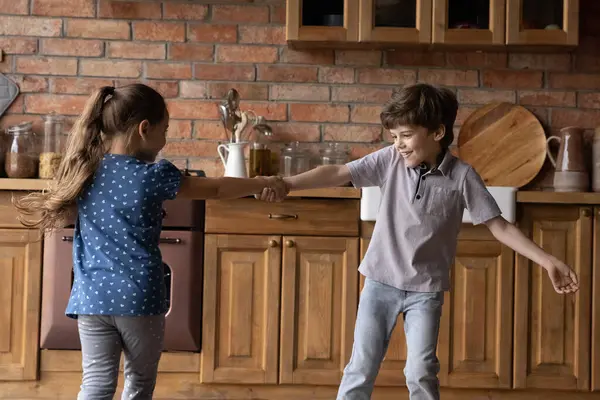 Alegre niños pequeños hermanos bailando girando alrededor de la cocina cogidos de la mano — Foto de Stock