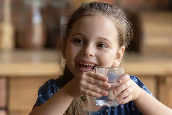 快乐的小女孩高兴地喝着玻璃杯里的凉水 — 图库照片