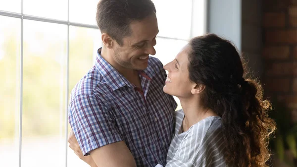 Feliz casal milenar abraçando perto da janela olhando nos olhos — Fotografia de Stock