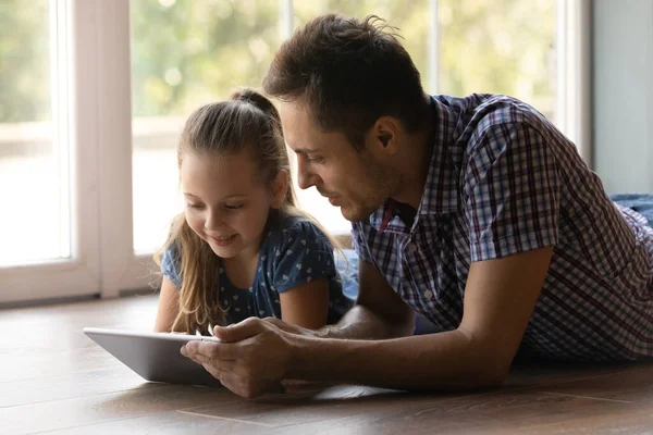 Little daughter and loving father reading book on tablet indoors — Stock Photo, Image