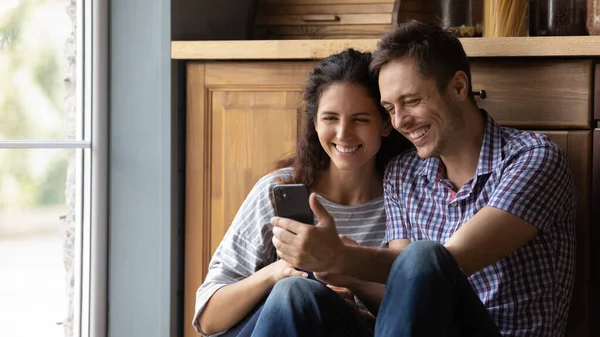 Feliz pareja milenaria abrazando mirando en la pantalla del teléfono celular viendo fotos — Foto de Stock