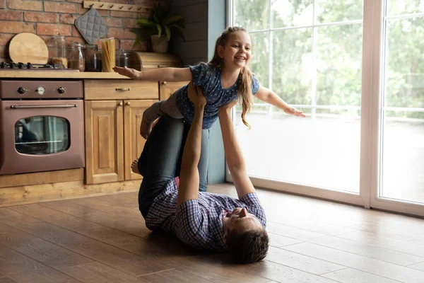 Jonge papa liggend op terug tillen junior dochter in de lucht — Stockfoto