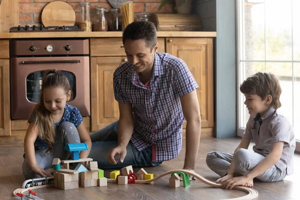 Gardien mâle construisant la gare de jouets avec deux enfants juniors — Photo