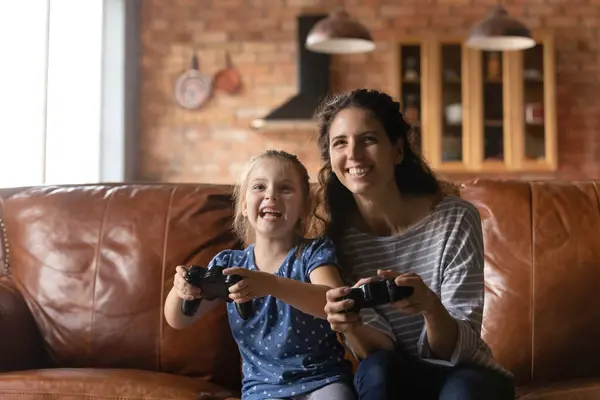 Millennial madre y pequeña hija relajarse en el interior jugando videojuego —  Fotos de Stock