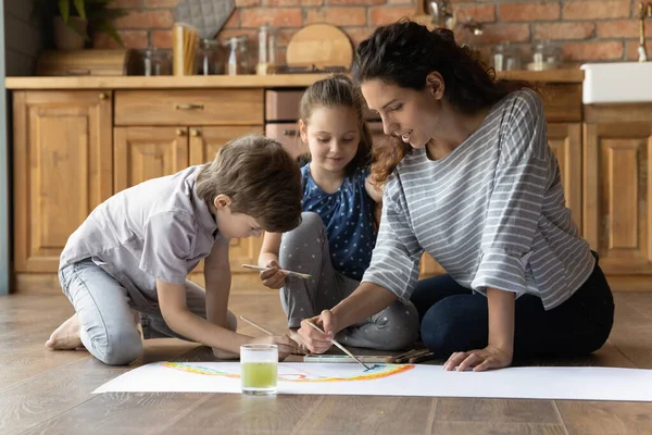 Geïnspireerd jong mam en twee kinderen schilderij schilderij op vloer — Stockfoto