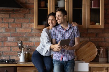 Evli çift mutfakta sarılıp tablet kullanarak mobilya seçiyor.