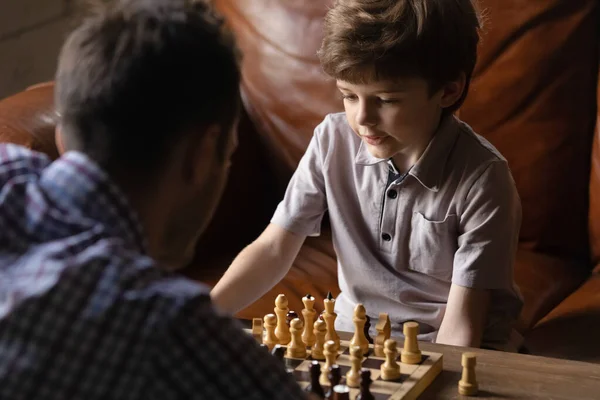 Pozorný chlapec junior žák hraje šachy s mladým trenérem — Stock fotografie