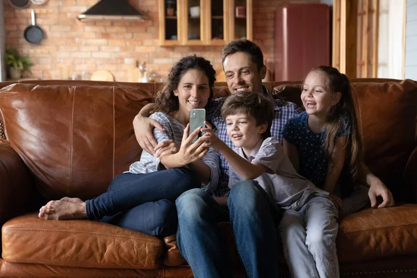 Счастливая семейная пара с маленькими детьми делают селфи по телефону — стоковое фото