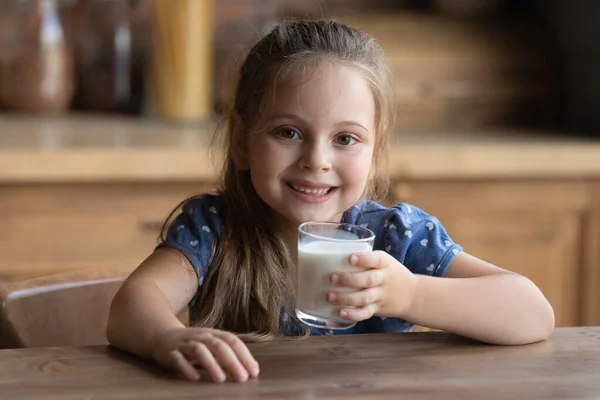 Friska liten flicka tittar på kameran håller glas mjölk — Stockfoto