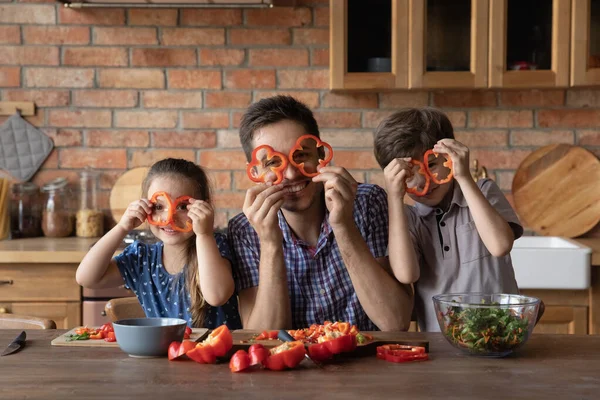 Χαρούμενος νεαρός μπαμπάς με παιδιά που φτιάχνει γυαλιά από γλυκό πιπέρι. — Φωτογραφία Αρχείου